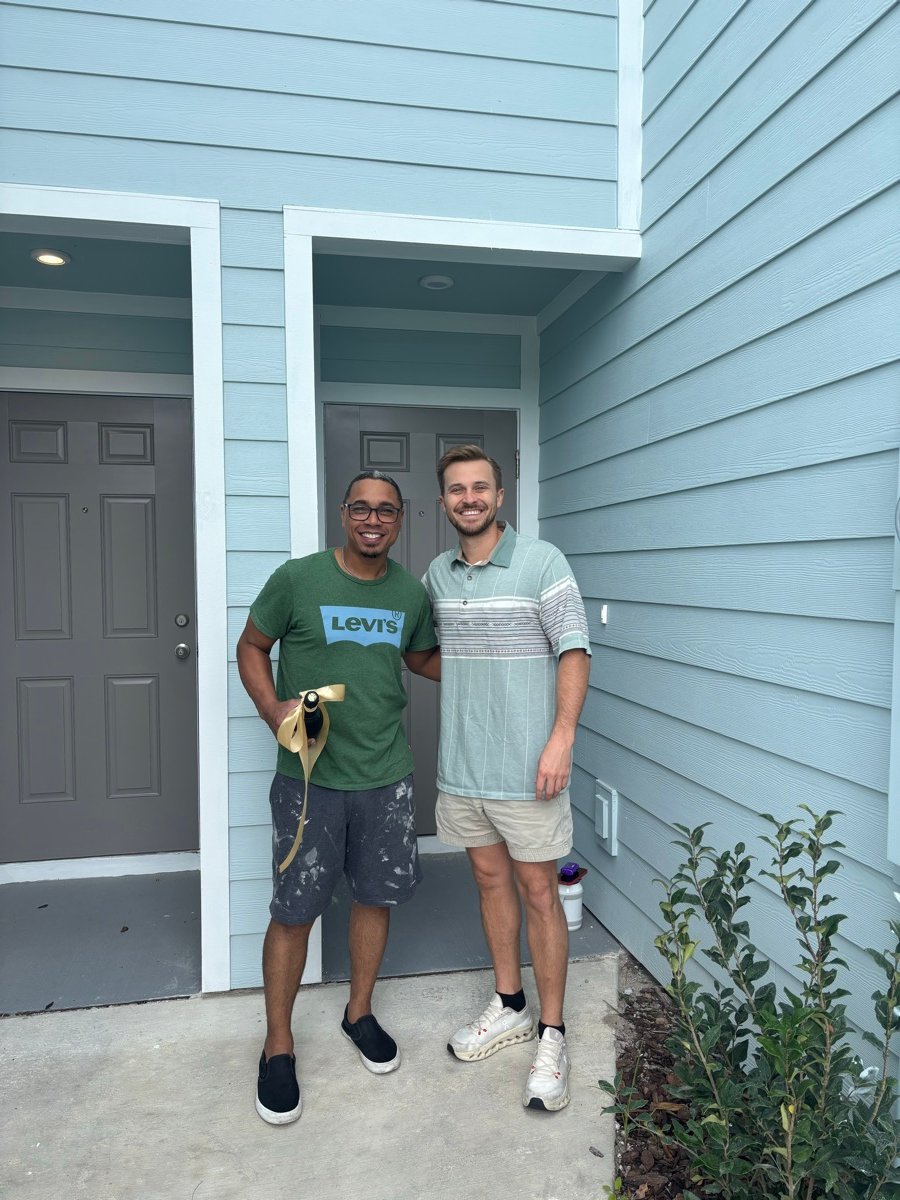 A client holding a ribboned bottle beside Rick outside his new front door