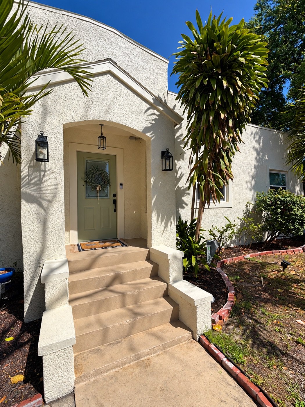 The same bungalow repainted cream with a sage green door and new lanterns