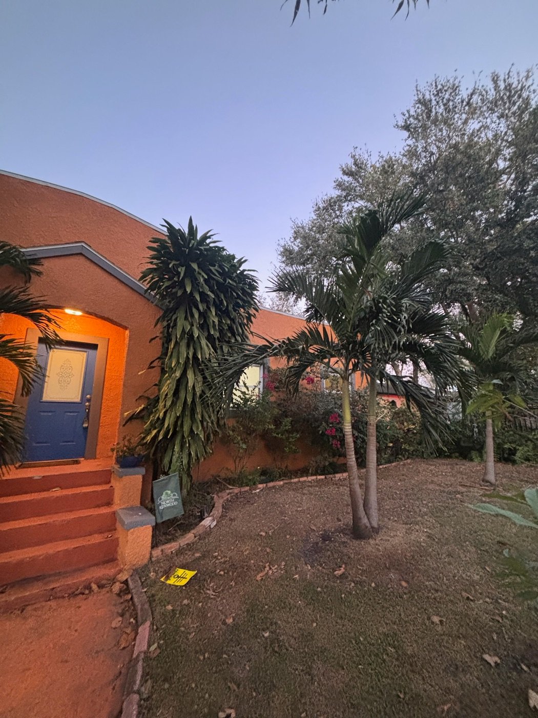 Orange stucco bungalow with a blue front door and overgrown yard