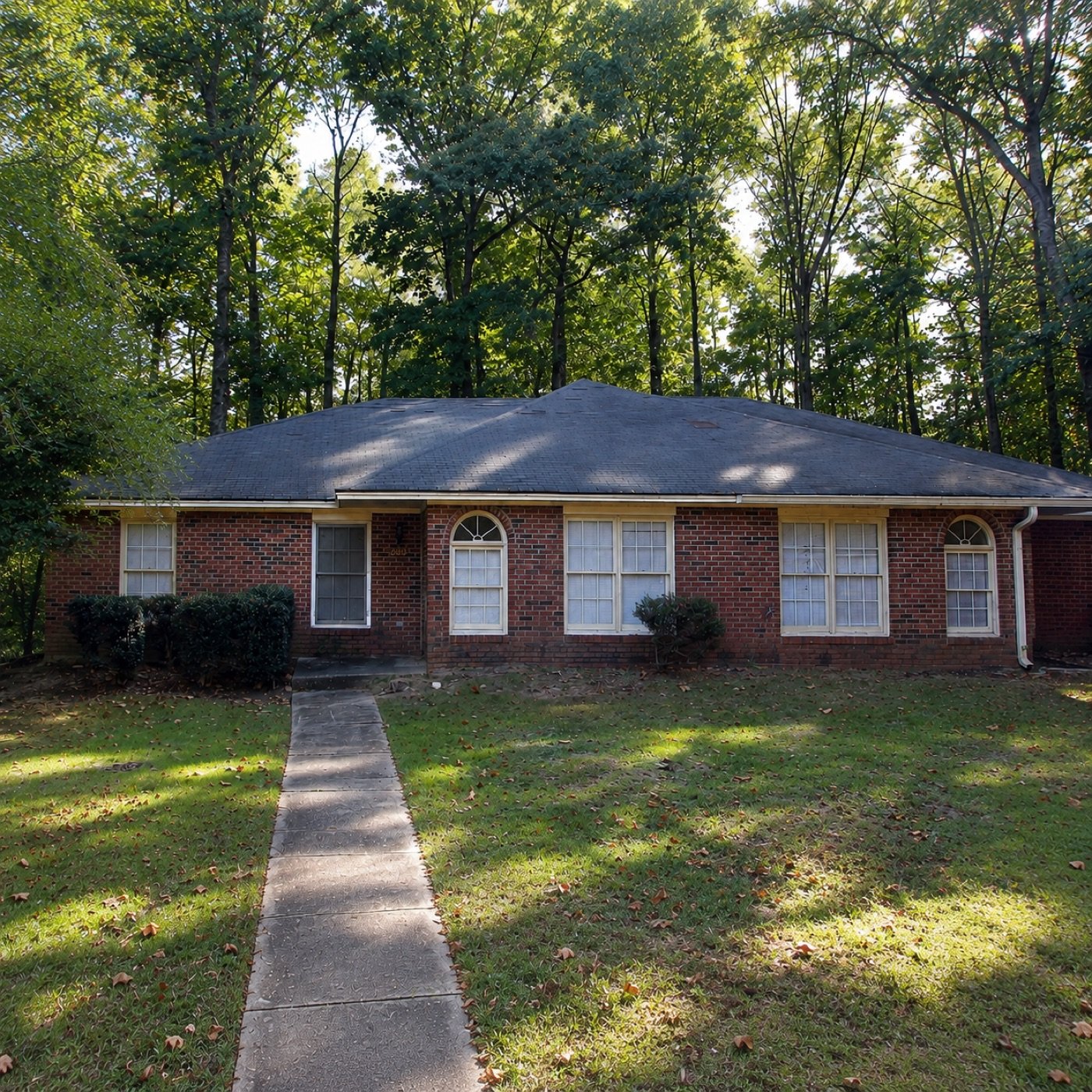 Brick duplex with arched windows, set among tall trees