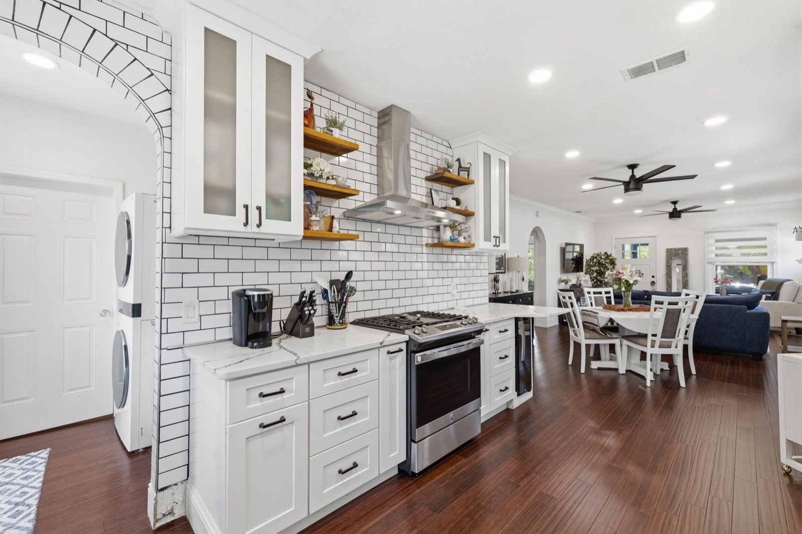 White kitchen with subway tile and open shelving, open to the dining and living room